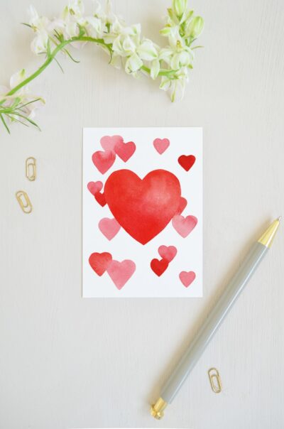 blanco ansichtkaart met groot rood hart van aquarel en daaromheen kleine rode hartjes