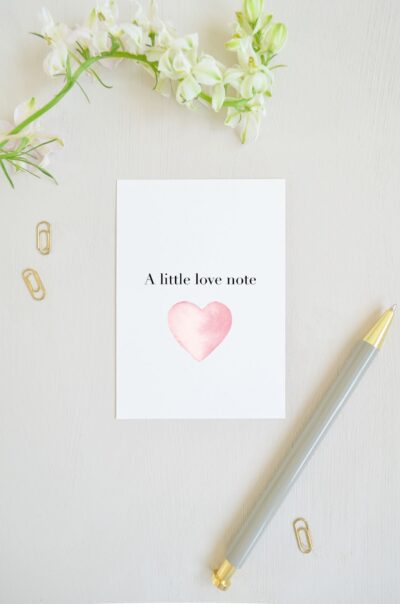 blanco ansichtkaart met groot roze hart van aquarel en op de voorkant de tekst 'a little love note', voor een klein liefdes briefje